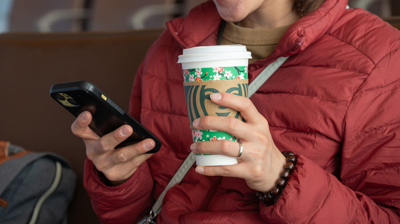Woman looking at her phone and holding a Starbucks cup