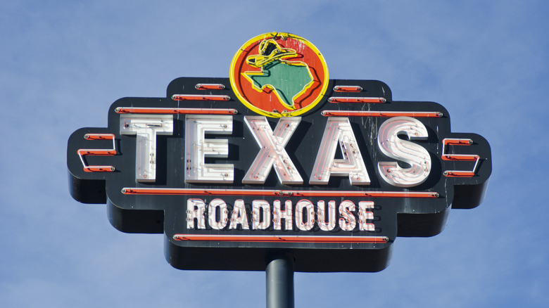 A Texas Roadhouse restaurant with a neon sign, photographed against a blue sky,