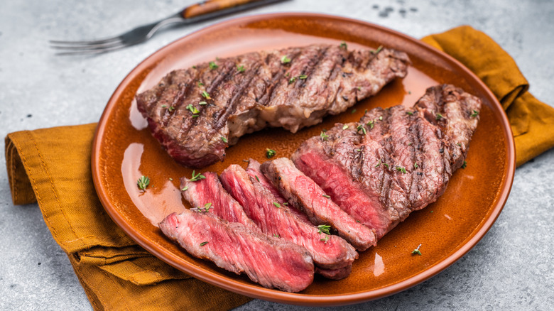 tender flat iron steak placed on a glossy brown plate next to a three pronged fork