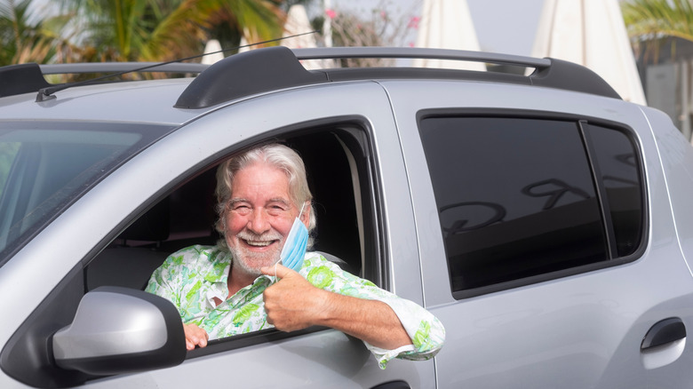 A senior man ready to drive his gray car looking at the camera from the window