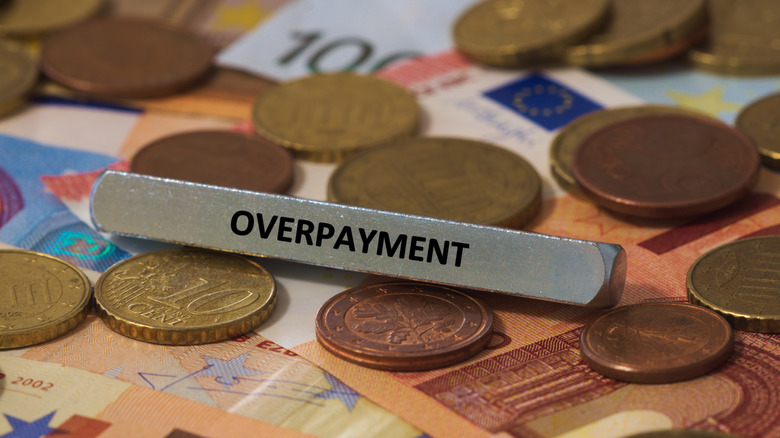 Coins and paper bills with a metal slug reading overpayment