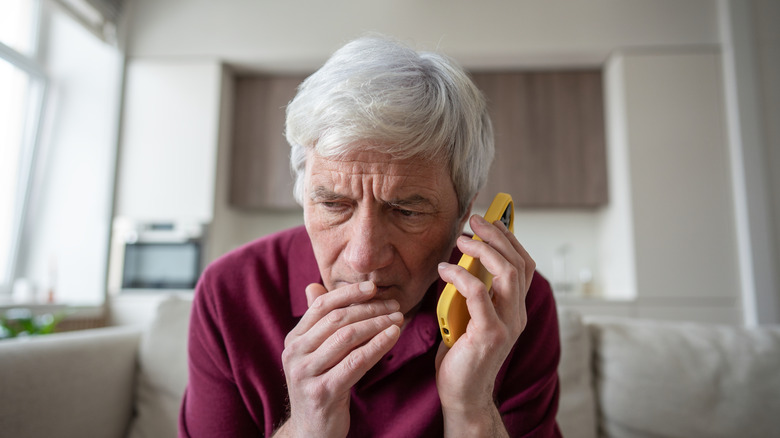 Suspicious white-haired senior listens to smart phone