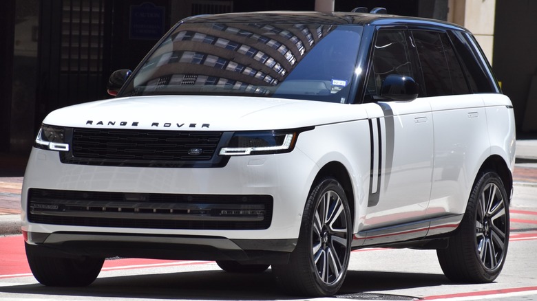 A white Range Rover SUV drives through a city street in bright daylight