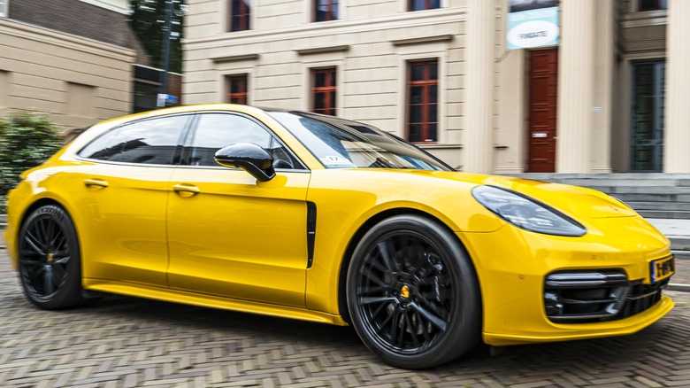 A bright yellow Porsche Panamera drives past historic buildings on a cobblestone street