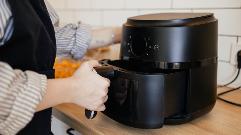 Unidentified person closing the basket of a black air fryer on a brown kitchen countertop