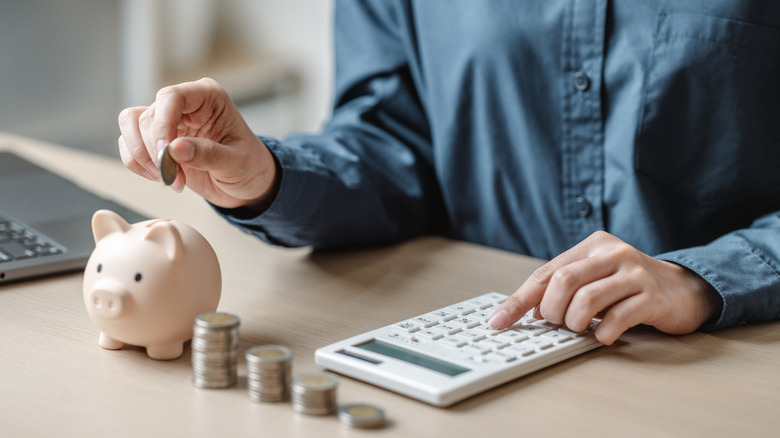 person using calculator and putting coins in piggy bank