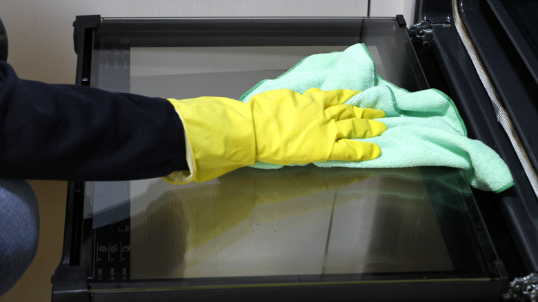 Gloves hands wiping an oven door with towel