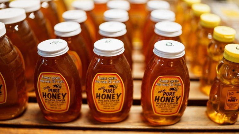 Jars of local honey arranged in rows on a shelf for sale.