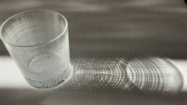 A highball glass with etched lines reflecting light on to a table