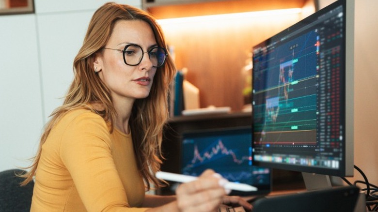 A woman wearing glasses looking at stock market reports and planning financial goals