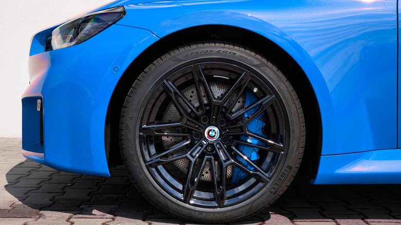 Close-up of a BMW's front wheel showing a black alloy rim, low-profile tire, and large performance brake caliper on a blue car