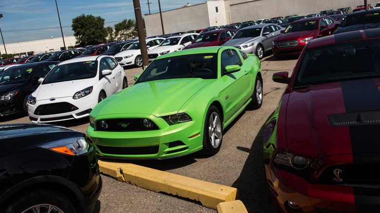 Bright green Ford Mustang parked diagonally in a crowded dealership lot, surrounded by rows of other cars