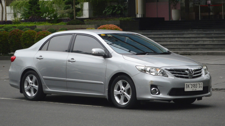 A side view of a silver 2013 Toyota Corolla driving down a street.