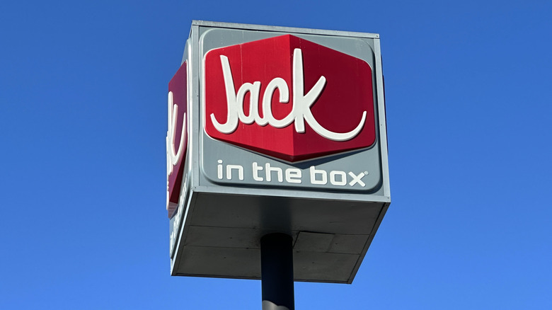 A Jack in the Box cube on a pole against a blue sky.