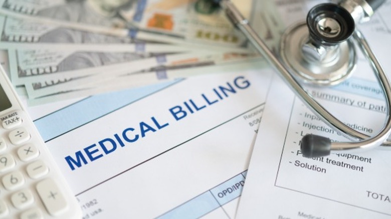 Money, a calculator, and a stethoscope piled on top of medical bills