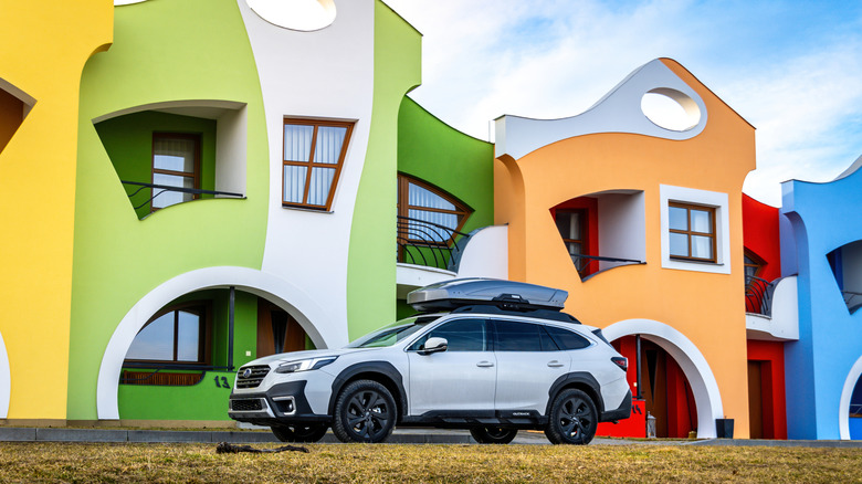 A white Subaru Outback parked in front of a row of funky, colorful houses.
