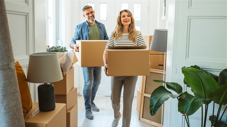 Two people smiling, carrying boxes