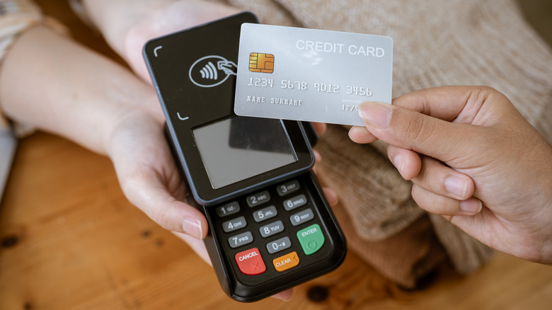 A close-up image of a customer tapping her credit card with a payment terminal or credit card machine at a cashier in a clothing store.