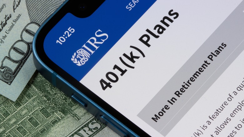 A smartphone opened to an irs article on 401(k) plans rests on hundred dollar bills