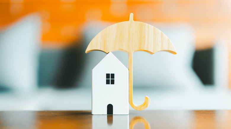 Model of umbrella with house on wooden table concept of the system of insurance.
