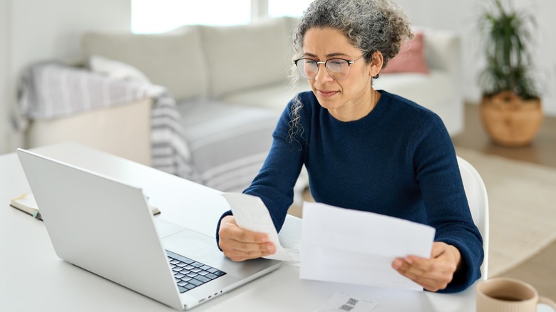 Mature woman examines invoices while seated in front of a laptop
