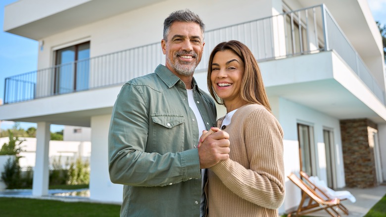 Happy mature couple embrace in front of modern-style house