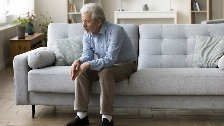 senior man sitting along on a couch looking sad