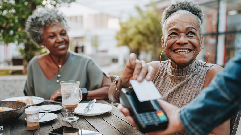 A senior woman paying for a meal on a patio with her credit card
