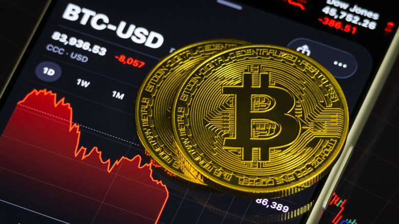 Two gold Bitcoins stacked up on a smartphone with an image of Bitcoin's falling stock chart on the screen.