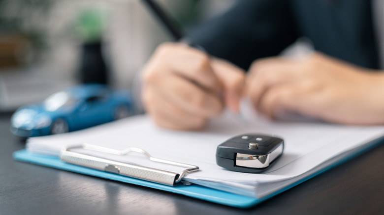 Person signing dealership paperwork.