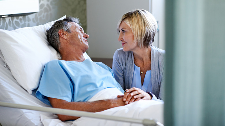 Man in hospital bed holding wife's hand
