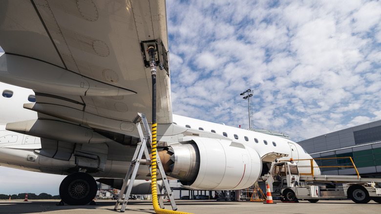 The underside of a small commercial jet parked at an airport terminal and getting refueled.