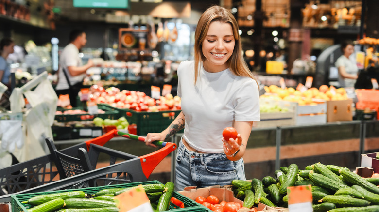 Young woman inspecting tomato at grocery store