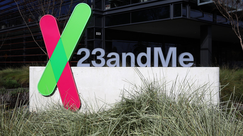 The 23andMe corporate headquarters sign, foregrounded by tufts of grass, with the 23andMe building in the background.