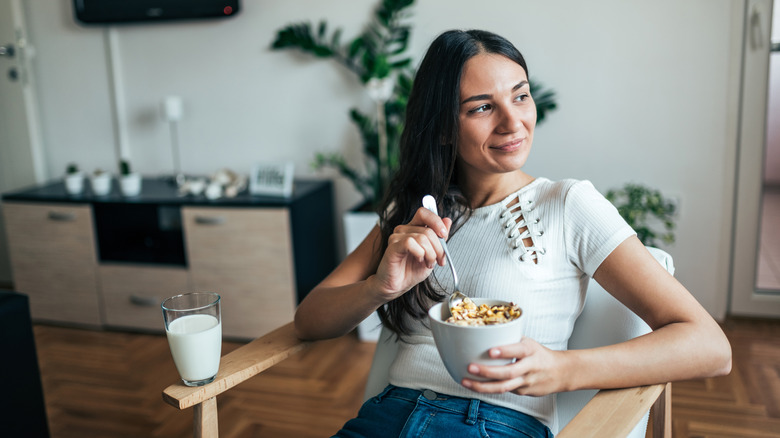 A young woman smiles as she eats cereal while sitting in armchair