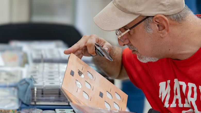 A coin collector inspects to details of a coin using a magnifying glass