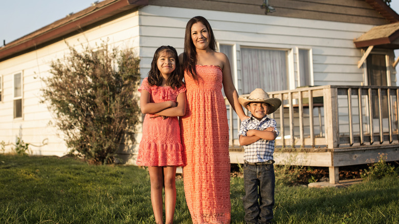 A woman and two children standing in front of a country home.