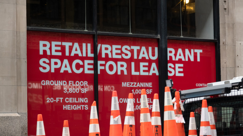 An Retail/restaurant space for lease, blocked by orange pylons, red signs advertising attributes in windows.