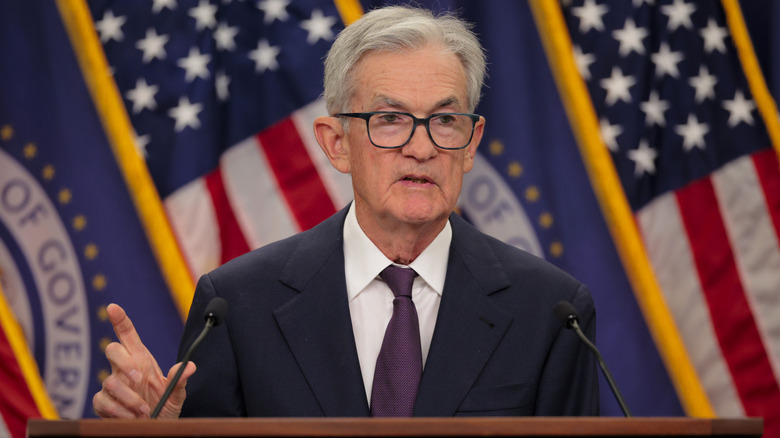 Fed Chair James Powell addresses rate cuts at micced podium in front of American flag display