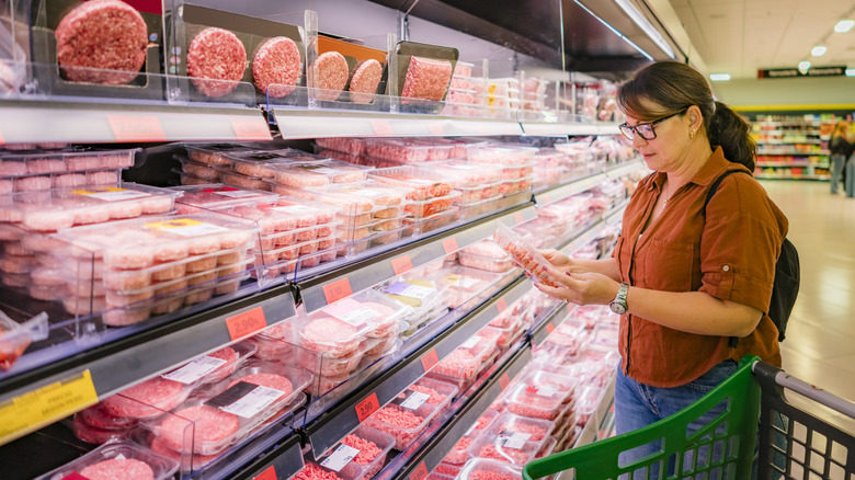 A woman looking at ground beef and burger patties in a store