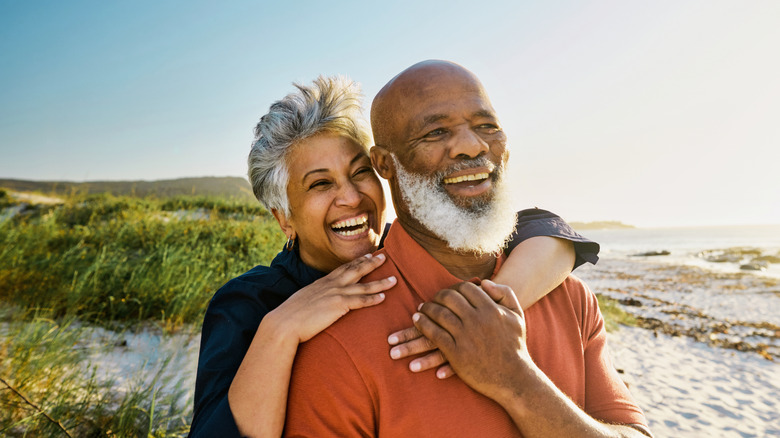 A beaming mature couple standing on a beach on a sunny day.