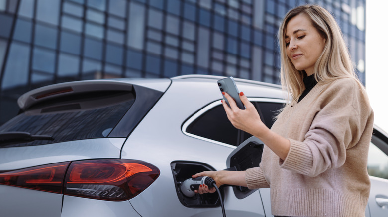 Young woman with smartphone waiting for car charging.