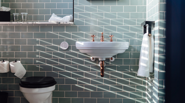 A bathroom with a tile wall, a sink, a toilet, and a mirror.
