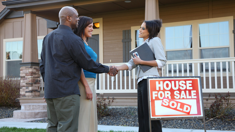 People shaking hands with a real estate agent outside a sold home