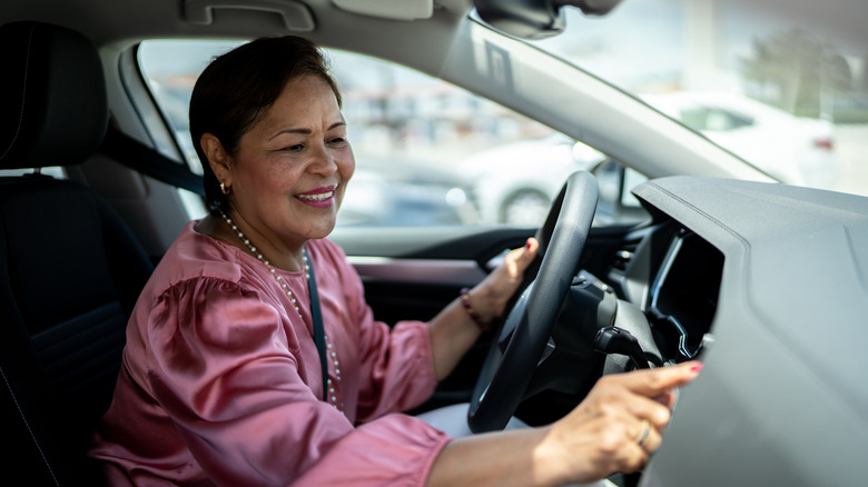 A smiling older woman adjusts a setting in her car