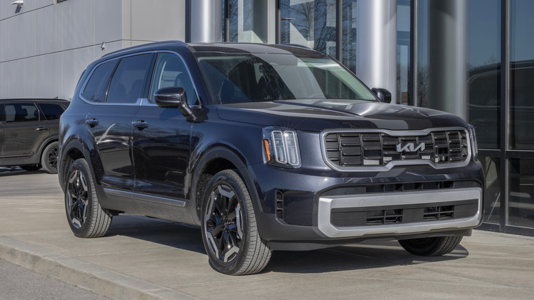 A dark 2025 Kia Telluride on a cement platform outside of a dealership