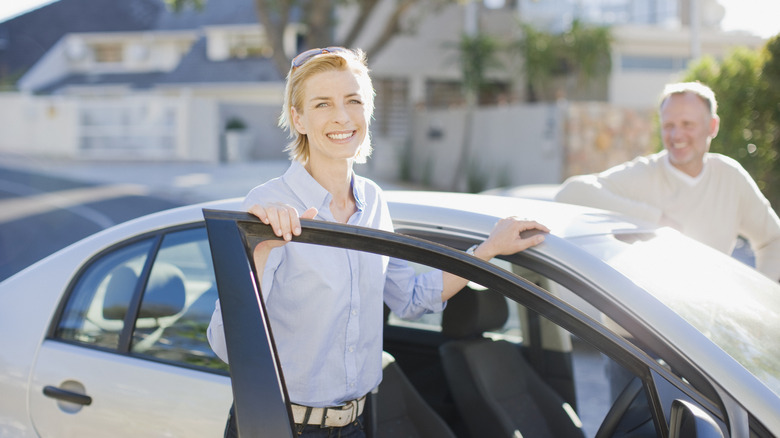 A smiling middle aged couple getting into a car together.