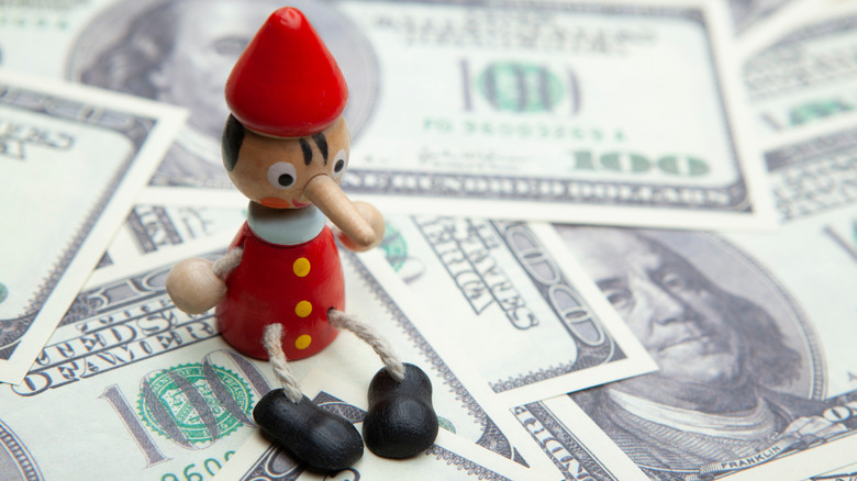 a Pinocchio toy sitting on a pile of $100 bills