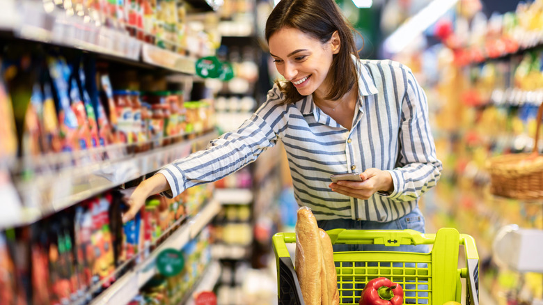 Smiling woman grabbing item to place in shopping cart