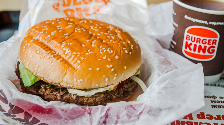 Burger King Whopper sitting in its rapper next to a drink